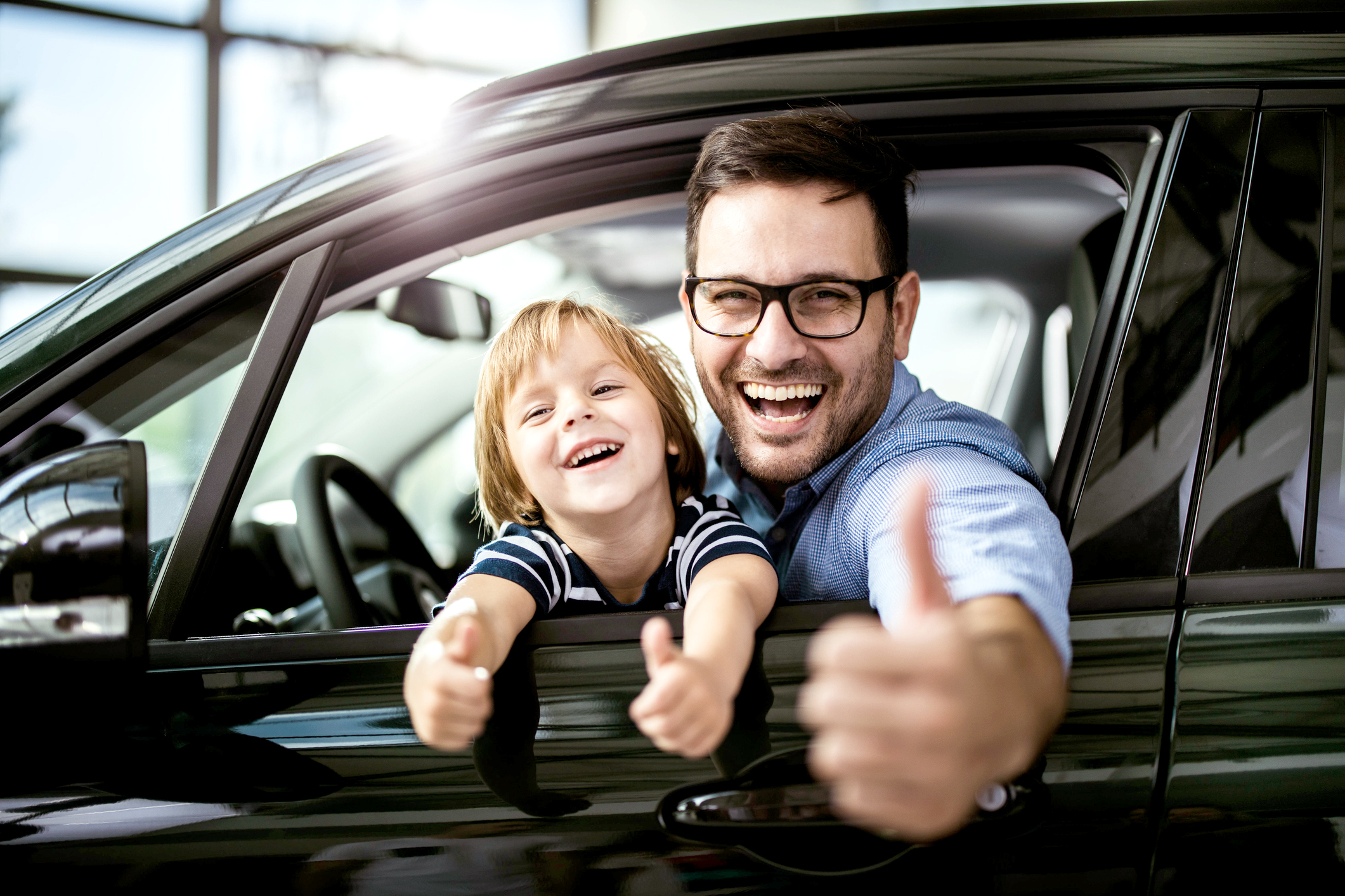 Feliz padre soltero e hijo probando un auto nuevo en una sala de exposición y mostrando el visto bueno